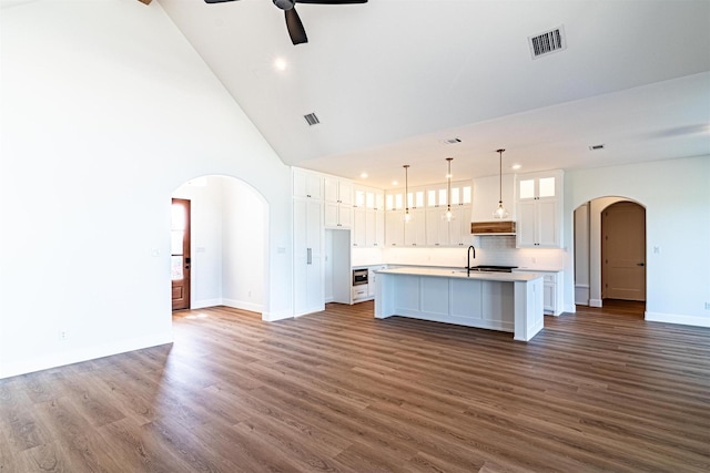 kitchen with hanging light fixtures, dark wood-type flooring, an island with sink, and white cabinets