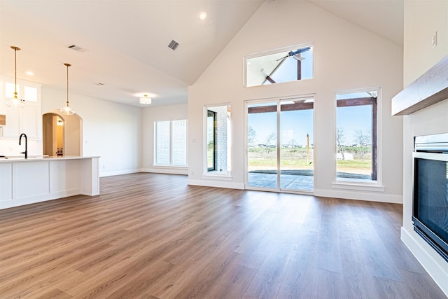 unfurnished living room featuring hardwood / wood-style floors, high vaulted ceiling, sink, and ceiling fan