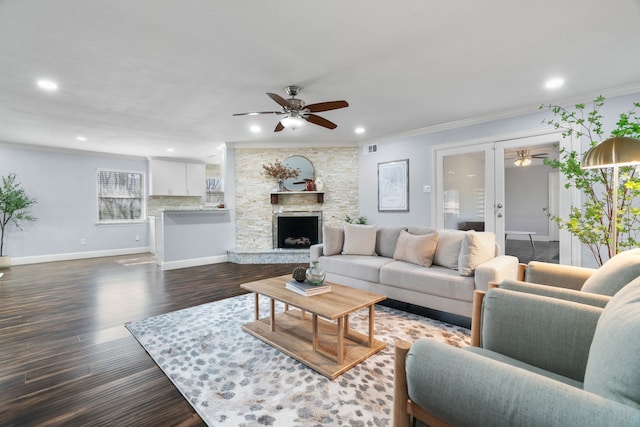 living room featuring ceiling fan, ornamental molding, dark hardwood / wood-style flooring, and a stone fireplace