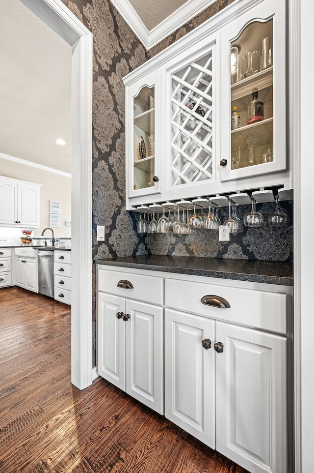 bar with dishwasher, white cabinetry, dark hardwood / wood-style floors, ornamental molding, and dark stone counters