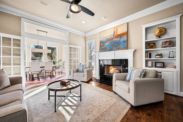 living room featuring crown molding, dark hardwood / wood-style flooring, built in features, ceiling fan, and a fireplace