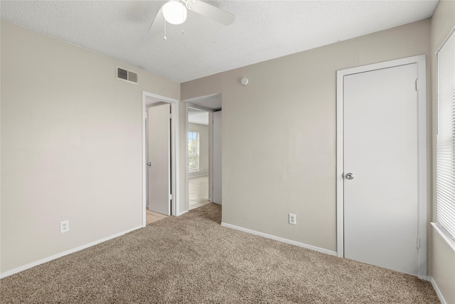 unfurnished bedroom with ceiling fan, light carpet, and a textured ceiling