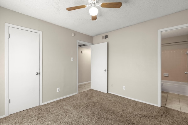 unfurnished bedroom featuring ceiling fan, light colored carpet, a textured ceiling, and ensuite bath