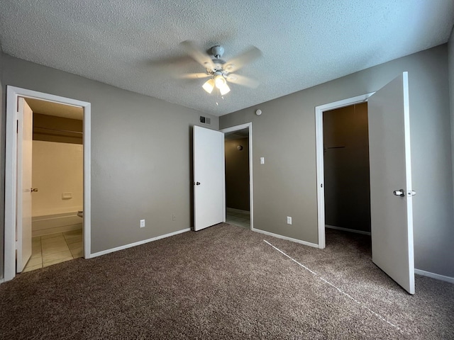 unfurnished bedroom featuring ensuite bathroom, a walk in closet, a textured ceiling, carpet floors, and ceiling fan