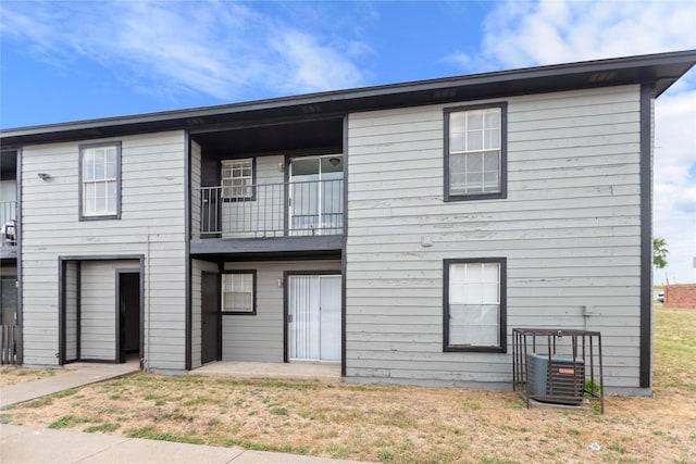 view of front of house with cooling unit, a front lawn, and a balcony