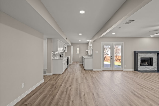 unfurnished living room featuring light hardwood / wood-style flooring, sink, a fireplace, and french doors