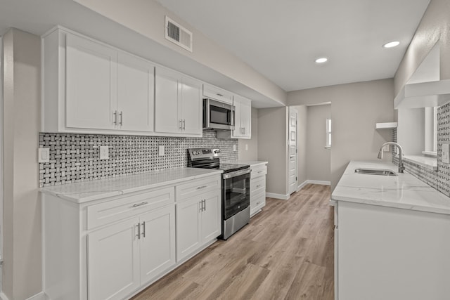 kitchen with tasteful backsplash, appliances with stainless steel finishes, sink, and white cabinets