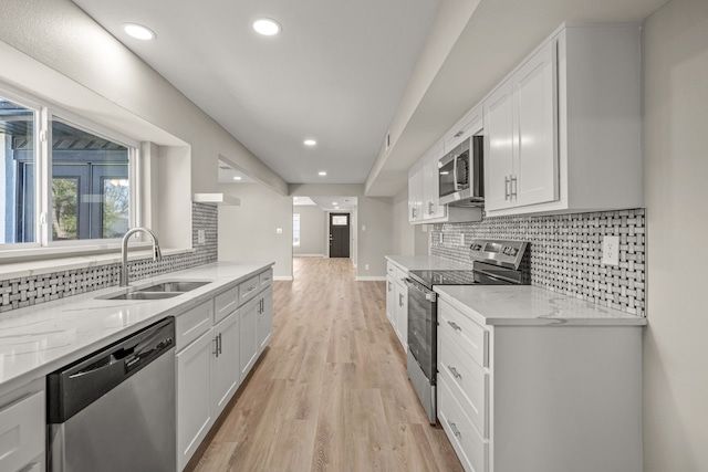 kitchen with white cabinetry, stainless steel appliances, light stone countertops, and sink