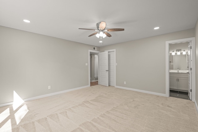 unfurnished bedroom with ceiling fan, sink, light carpet, and ensuite bath