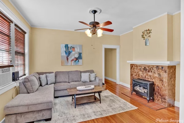 living room with hardwood / wood-style floors, crown molding, ceiling fan, and a wood stove