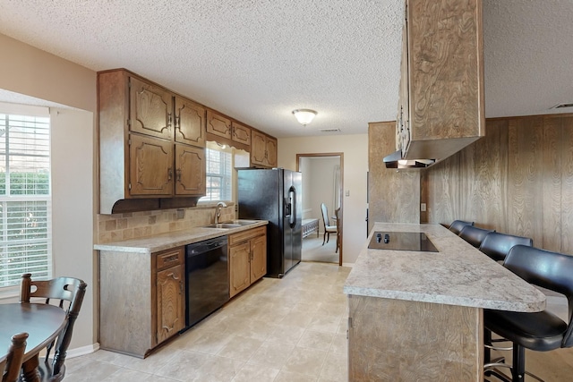 kitchen featuring sink, wooden walls, black appliances, a kitchen bar, and decorative backsplash