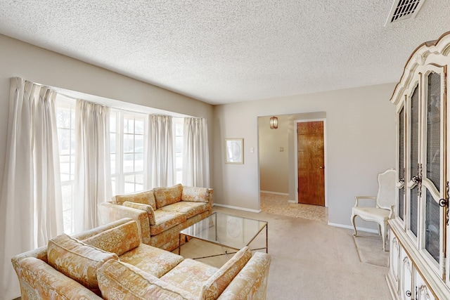 living room featuring light colored carpet, visible vents, a textured ceiling, and baseboards