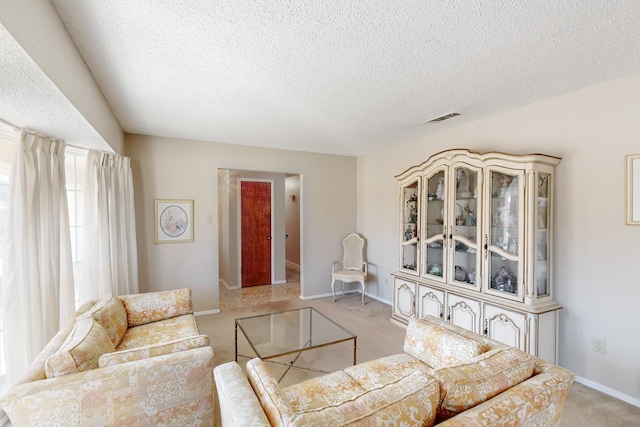 living room featuring a textured ceiling, baseboards, visible vents, and light colored carpet