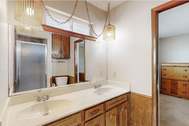 bathroom featuring a stall shower, a sink, toilet, and double vanity