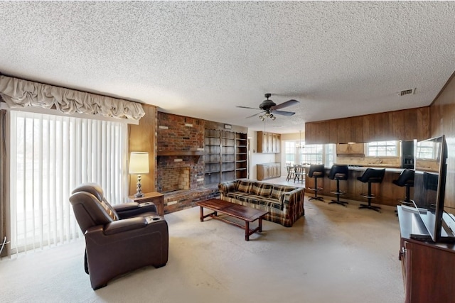 living room featuring ceiling fan, a brick fireplace, and a textured ceiling