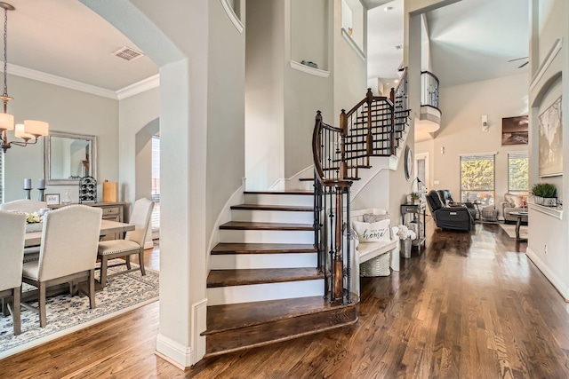 stairway featuring hardwood / wood-style flooring, a towering ceiling, crown molding, and a notable chandelier