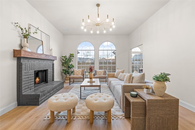 living room featuring an inviting chandelier, a brick fireplace, and light wood-type flooring