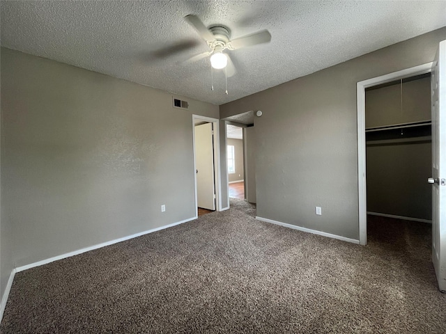 unfurnished bedroom featuring ceiling fan, dark colored carpet, a textured ceiling, a walk in closet, and a closet