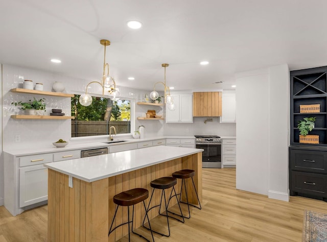 kitchen with sink, stainless steel gas stove, white cabinets, a kitchen island, and decorative light fixtures