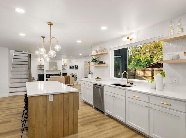 kitchen with sink, light hardwood / wood-style flooring, hanging light fixtures, dishwasher, and white cabinets