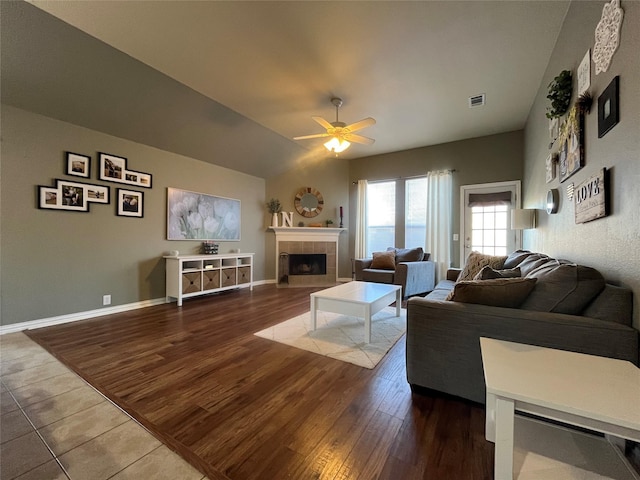 living room with vaulted ceiling, ceiling fan, a tiled fireplace, and hardwood / wood-style floors