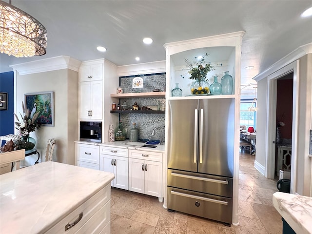 kitchen with stainless steel refrigerator, white cabinetry, backsplash, hanging light fixtures, and ornamental molding