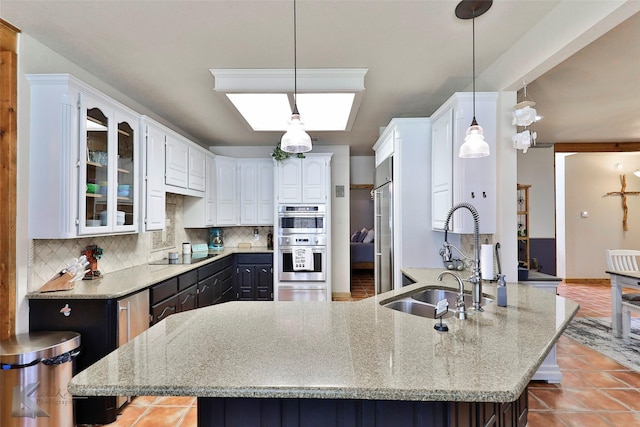 kitchen with sink, backsplash, stainless steel appliances, white cabinets, and decorative light fixtures