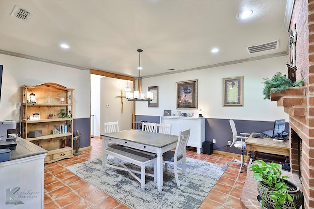 dining room with crown molding, a brick fireplace, light tile patterned floors, and a notable chandelier