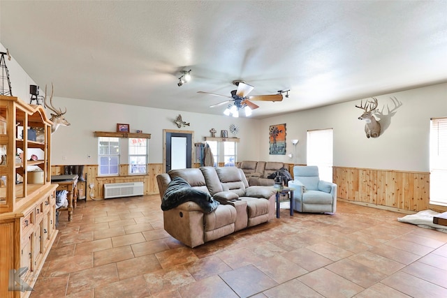 living room featuring ceiling fan, wooden walls, and a textured ceiling