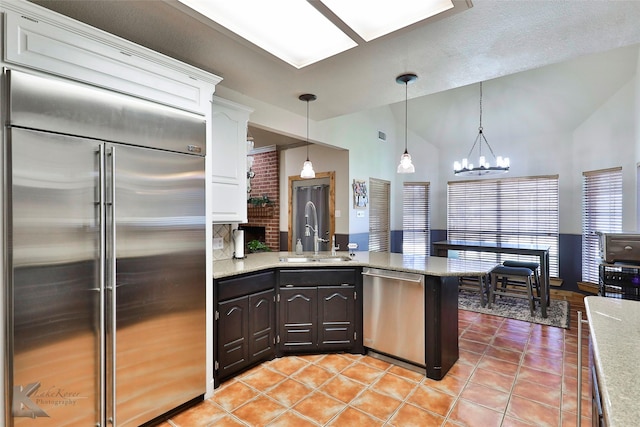 kitchen featuring vaulted ceiling, appliances with stainless steel finishes, sink, white cabinets, and light tile patterned floors