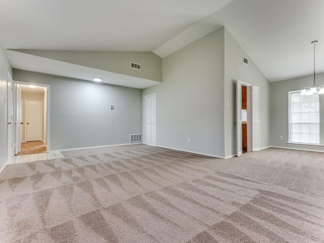 carpeted spare room with an inviting chandelier and high vaulted ceiling