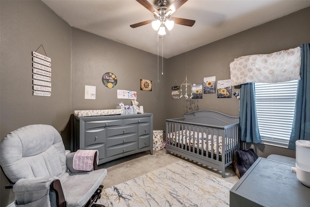 bedroom with a crib, light colored carpet, and ceiling fan