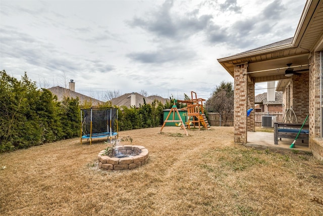 view of jungle gym with a trampoline, a yard, central AC, a patio, and an outdoor fire pit