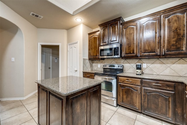 kitchen with tasteful backsplash, a center island, stainless steel appliances, light stone countertops, and dark brown cabinets