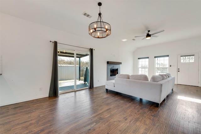 living room with dark wood-type flooring, ceiling fan with notable chandelier, a tile fireplace, and a wealth of natural light