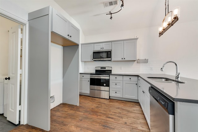 kitchen featuring sink, hardwood / wood-style floors, stainless steel appliances, decorative backsplash, and decorative light fixtures