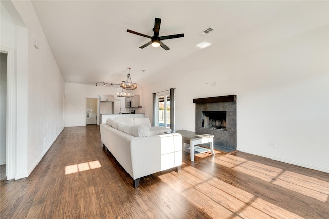 living room with ceiling fan with notable chandelier, rail lighting, hardwood / wood-style floors, and a tile fireplace