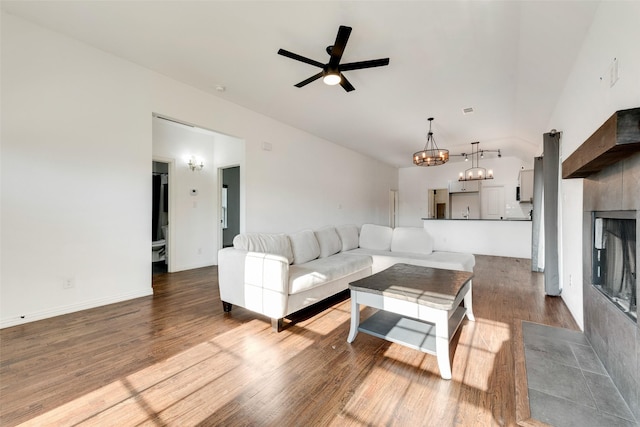 living room with a tiled fireplace, hardwood / wood-style flooring, ceiling fan with notable chandelier, and lofted ceiling