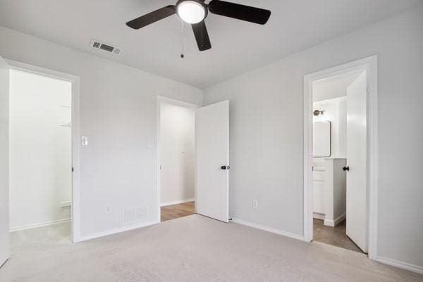 unfurnished bedroom with ceiling fan, light colored carpet, and ensuite bath