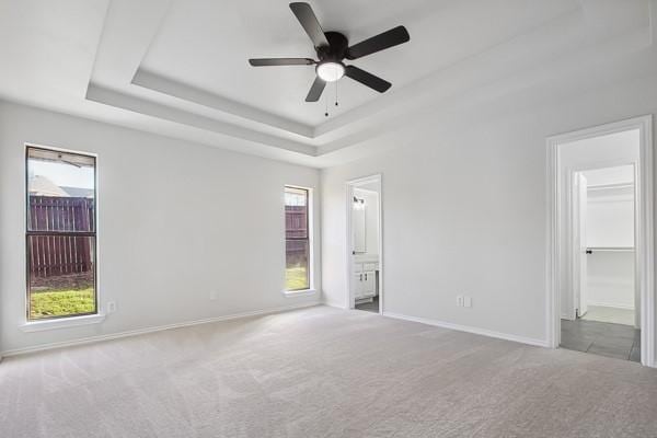 unfurnished room with light carpet, ceiling fan, and a tray ceiling