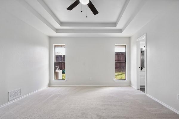 carpeted spare room with a tray ceiling and ceiling fan