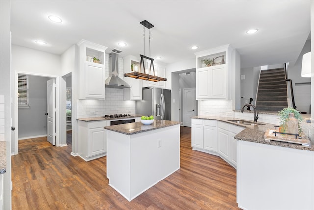 kitchen featuring sink, appliances with stainless steel finishes, white cabinetry, decorative light fixtures, and wall chimney exhaust hood