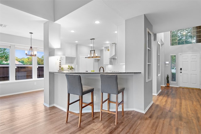 kitchen featuring a breakfast bar, white cabinets, dark hardwood / wood-style flooring, kitchen peninsula, and wall chimney exhaust hood