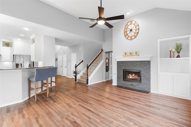 living room featuring ceiling fan, lofted ceiling, a fireplace, and light hardwood / wood-style floors