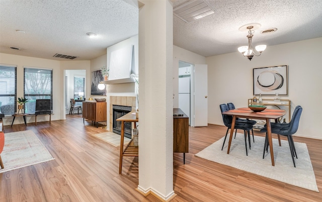 dining area featuring an inviting chandelier, a tile fireplace, light hardwood / wood-style flooring, and a textured ceiling