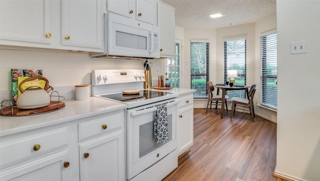 kitchen with a textured ceiling, white cabinets, white appliances, and light hardwood / wood-style flooring