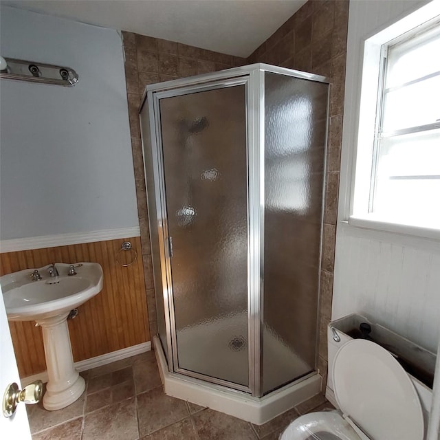 bathroom with tile patterned flooring, toilet, wood walls, and a shower with shower door