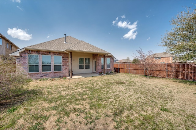 back of house with brick siding, fence, roof with shingles, a lawn, and a patio