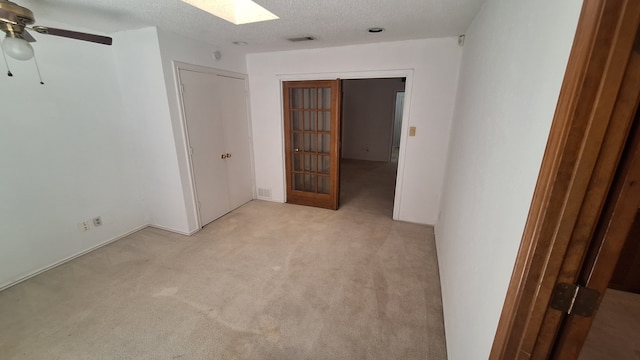 empty room featuring ceiling fan, light colored carpet, a skylight, and a textured ceiling