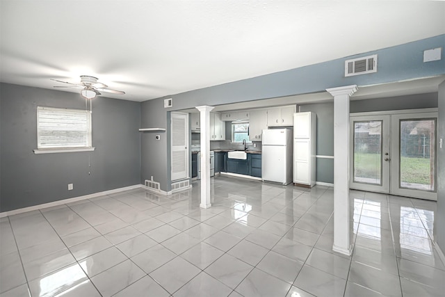 unfurnished living room featuring light tile patterned flooring, a healthy amount of sunlight, and ornate columns